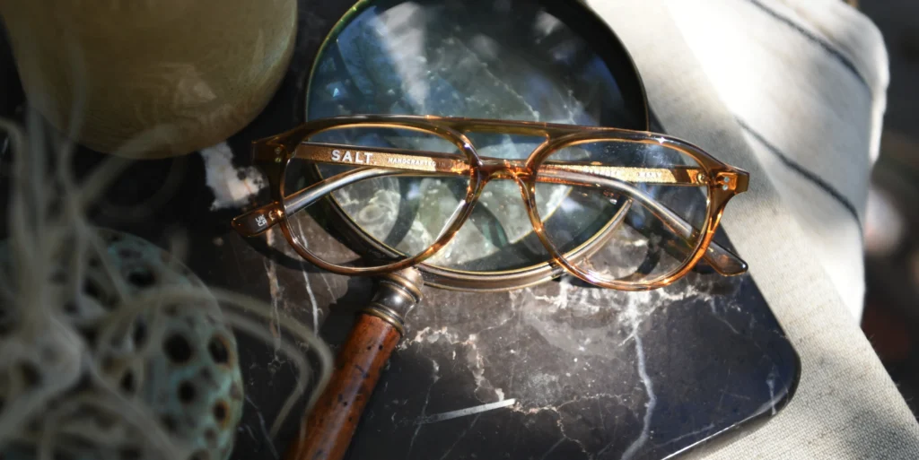 Tortoiseshell glasses resting on a magnifying glass over dark marble