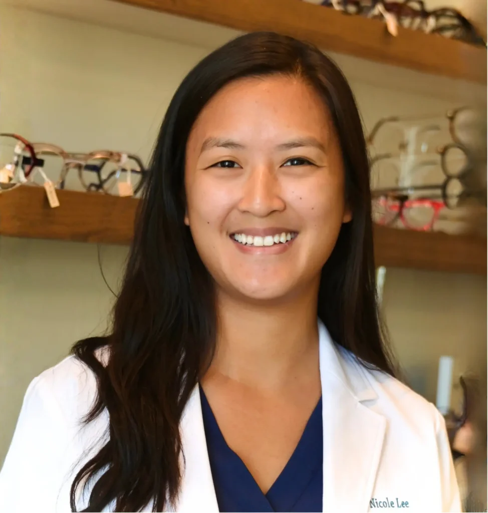 Dr. Nicole Lee, optometrist, smiling in a white coat in front of the frame wall