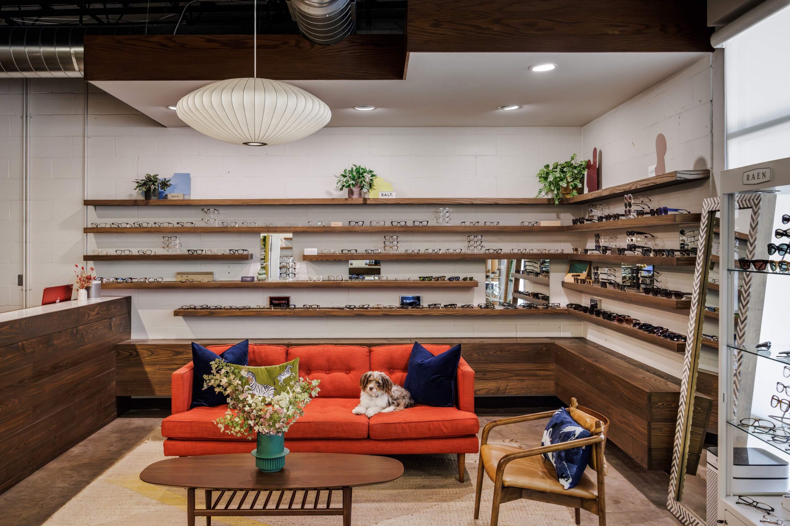 Look + See Vision Care eyewear gallery and seating area with a red-orange sofa and wood shelving