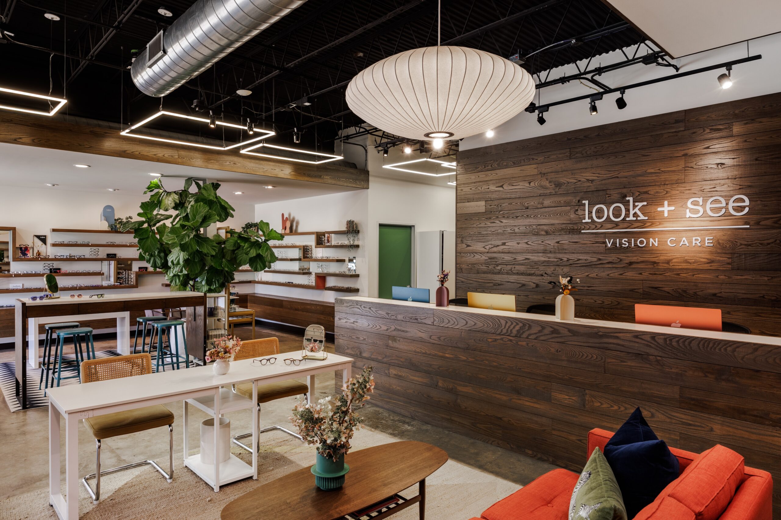 Look + See Vision Care reception and eyewear gallery with a wood-paneled wall, white counter and orange sofa