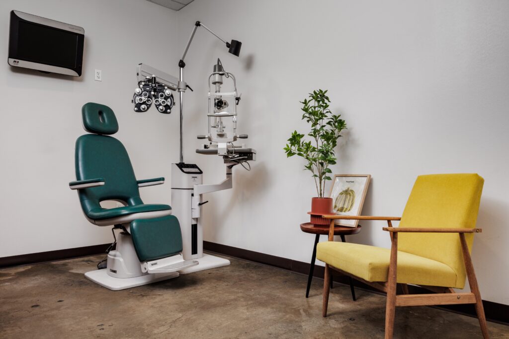 Look + See exam room with a green exam chair, phoropter and a yellow armchair