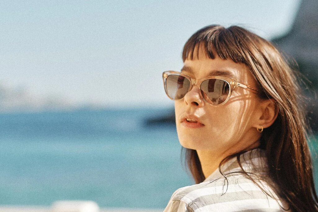 Woman with bangs wearing SALT. sunglasses with translucent tan frames, looking out over the water