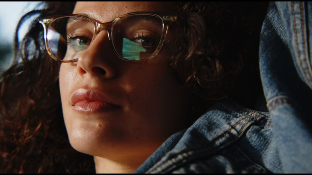 Close-up of a woman with curly hair wearing SALT. tortoiseshell glasses and a denim jacket